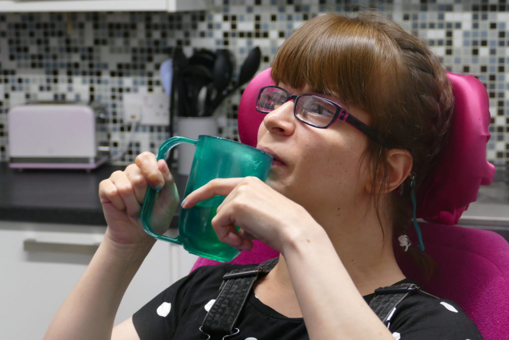 A young woman wearing glasses taking a sip from a green cup.