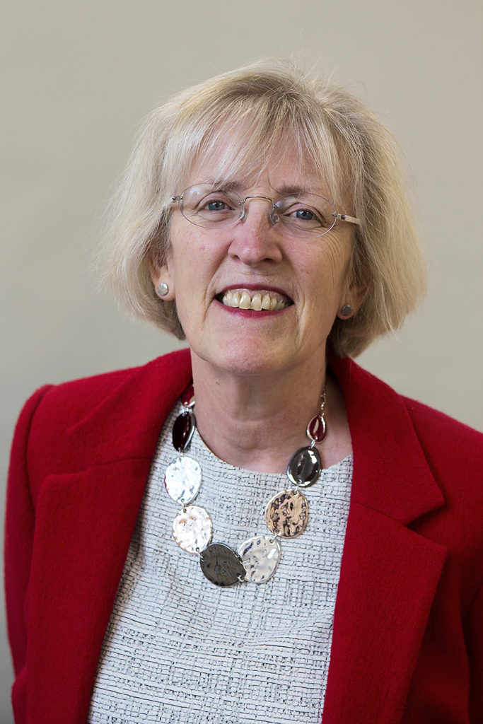 A headshot of Pat Dyson, a white woman wearing glasses and a red blazer.