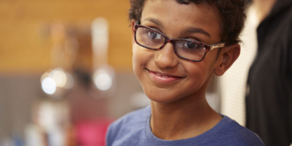 A young mixed race boy wearing glasses smiles at the camera.