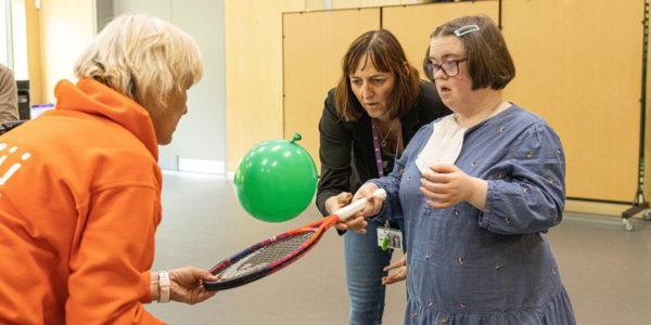 a woman hits a green balloon with a tennis racket