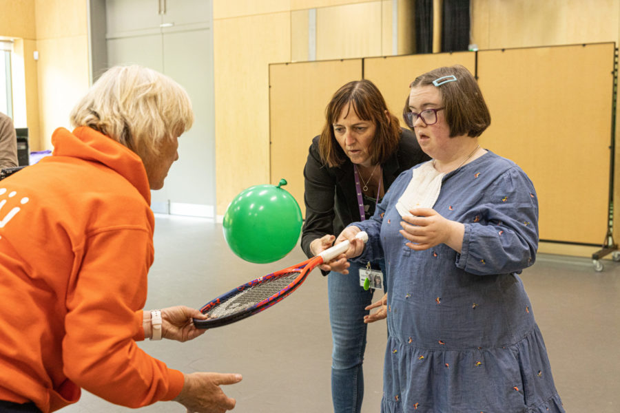 a woman hits a green balloon with a tennis racket