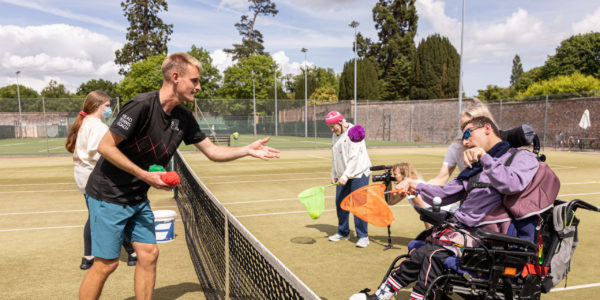 A man throws a ball to a woman in a wheelchair on the other side of a tennis net