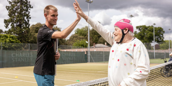 Two people high five over a tennis court net.