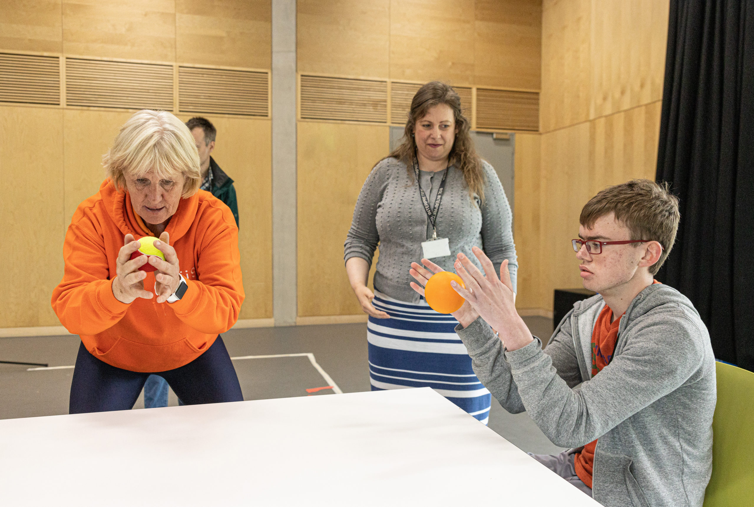 a boy drops an orange ball onto a table next to two women
