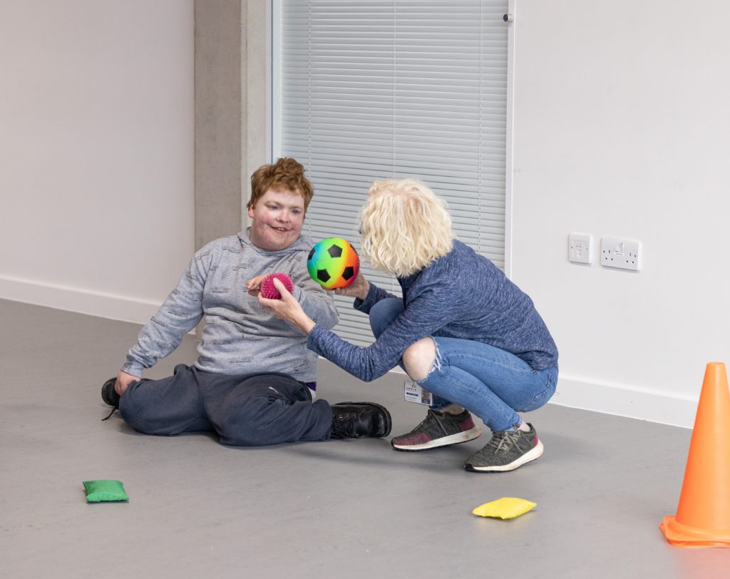 A woman and a boy are sitting on the ground and holding footballs