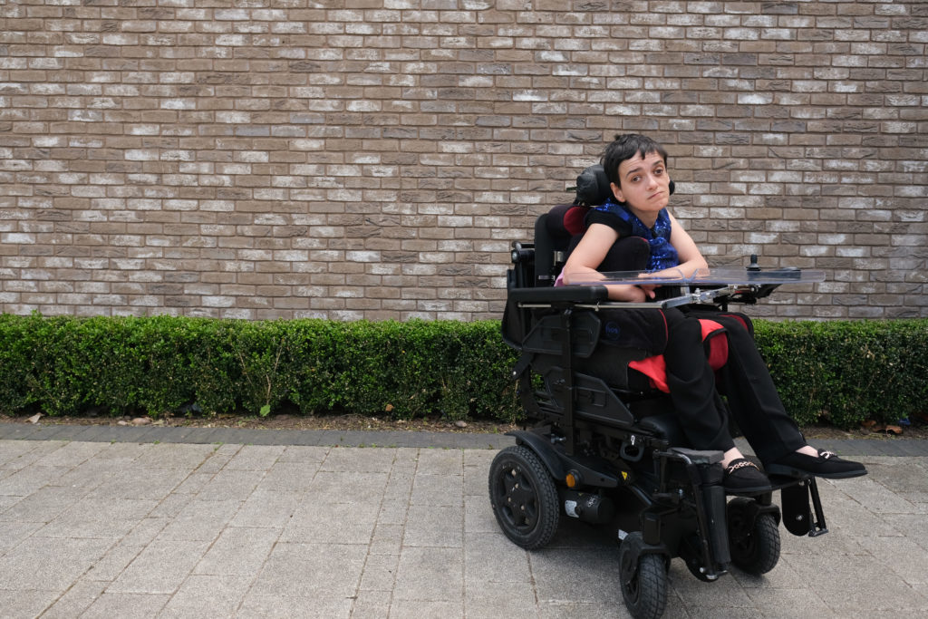 Jade, a woman with short hair, in a wheelchair, in front of a brick wall.