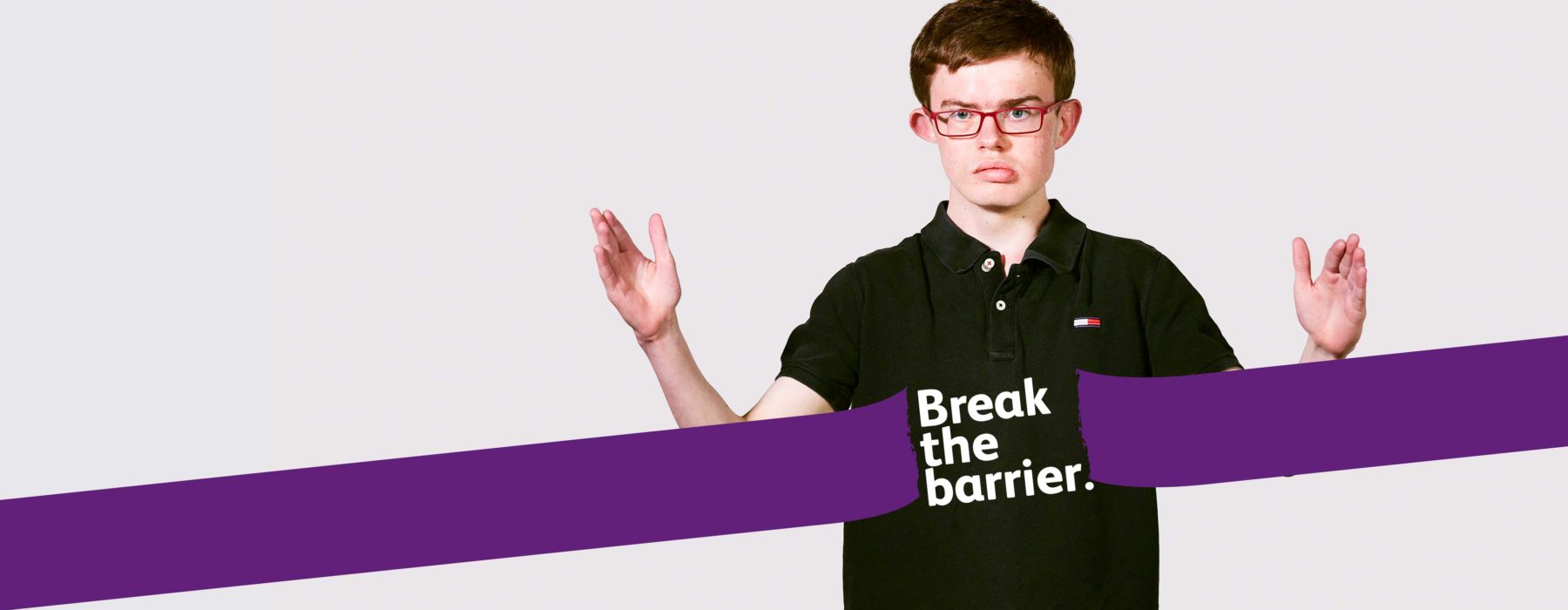 Young man wearing glasses signing 'break' in BSL. There is a purple banner over his torso with the words 'break the barrier' on his stomach.