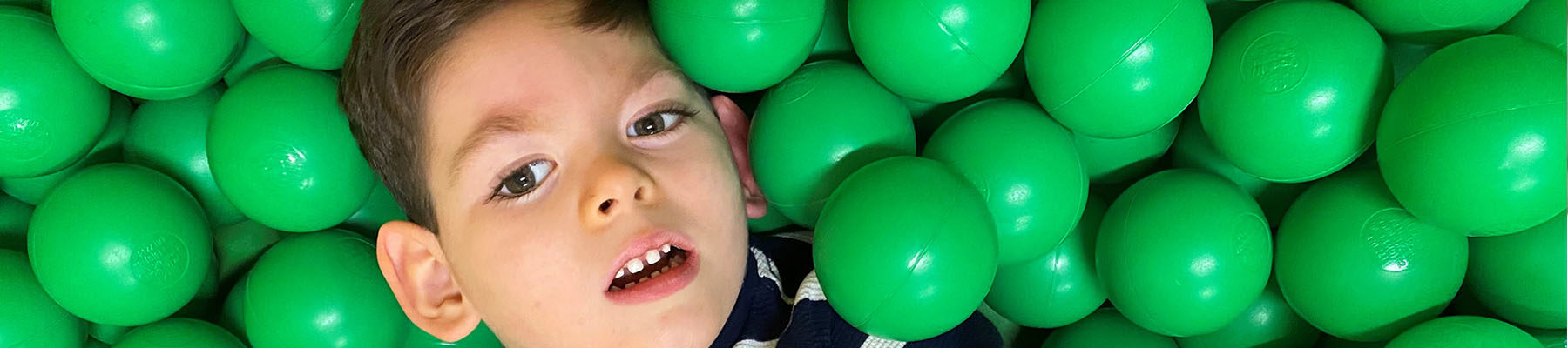 A young boy in a ball pond surrounded by green balls