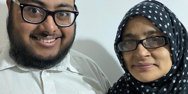 Saihan, a young man in glasses, with his mum Firdush, a woman wearing glasses and a hijab, both smiling to camera.