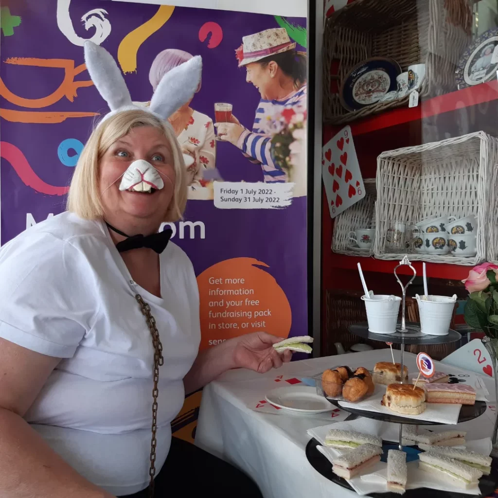 Julia, a woman with blonde hair wearing rabbit ears and a rabbit nose, picking up a sandwich at her Sensational Tea Party.
