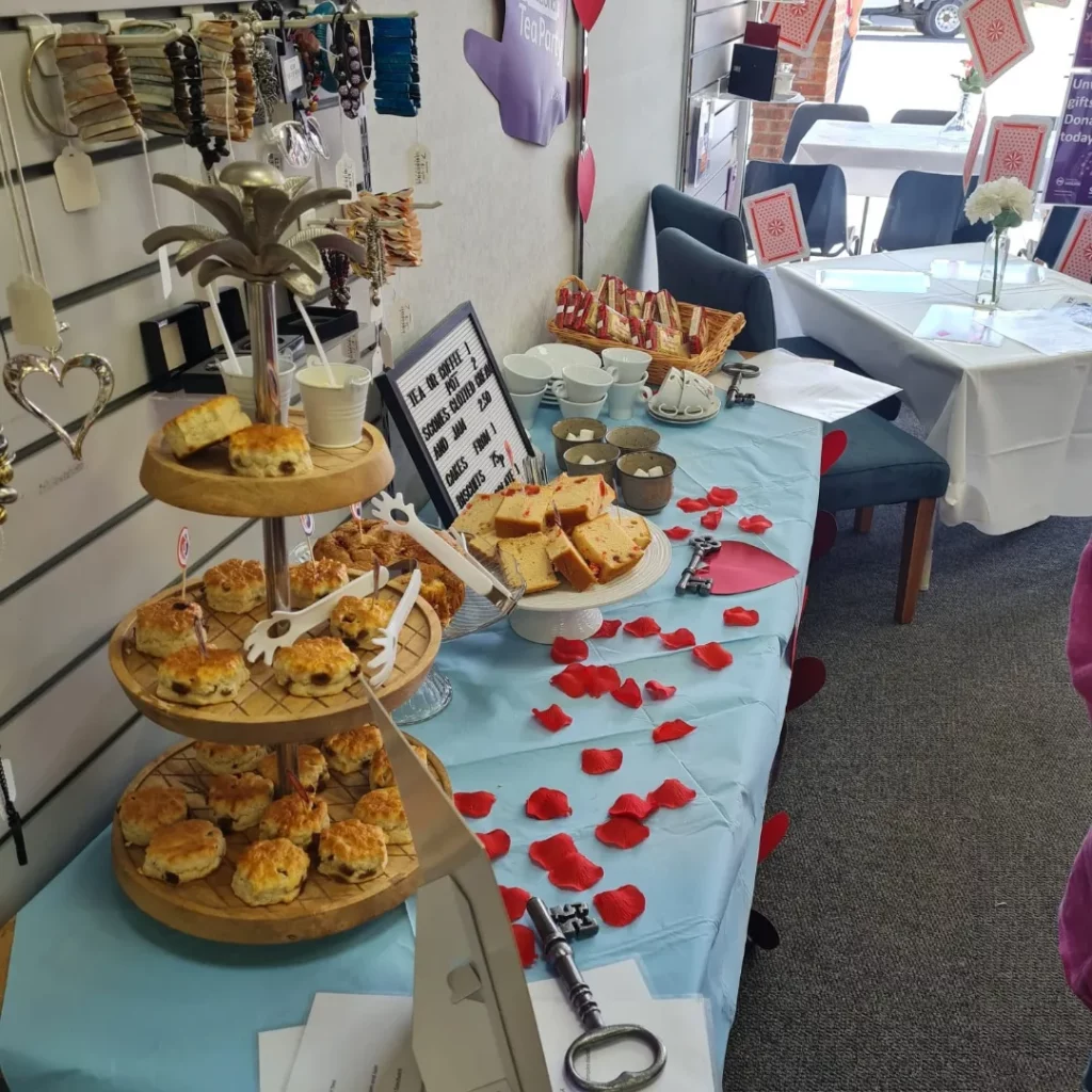 A table decorated with rose petals, keys and hearts, displaying cake, scones and teacups.