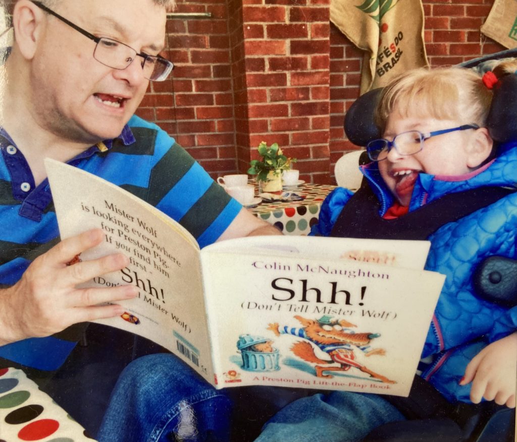 A man reading a story to a girl in a wheelchair