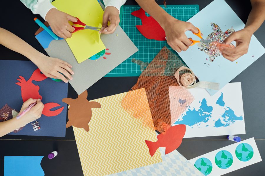 Three pairs of hands photographed from above, cutting colourful pieces of paper into the shapes of fish and turtles.