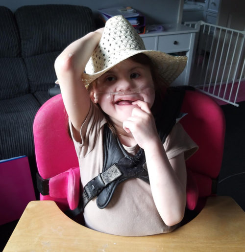 Annalise sitting in her chair at a table wearing a hat