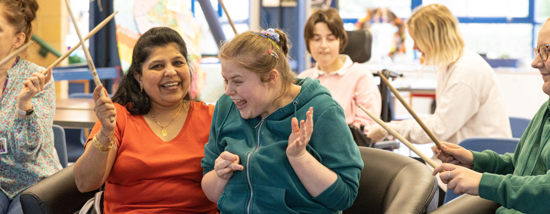 A young woman and her support worker laughing while taking part in a drumming session.