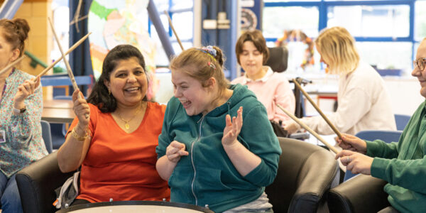 A young woman and her support worker laughing while taking part in a drumming session.