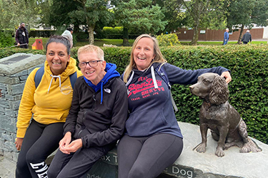 Two women and a man sitting next to a bronze statue of a dog