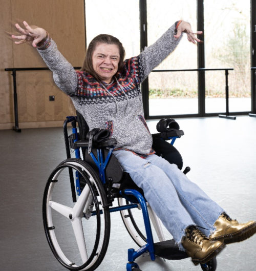 A young woman sitting in a wheelchair with her arms raised