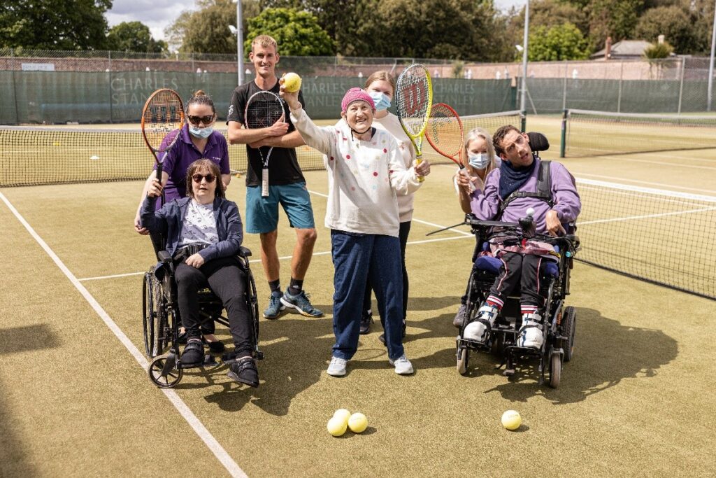 A group of people standing on a tennis court holding up their tennis rackets