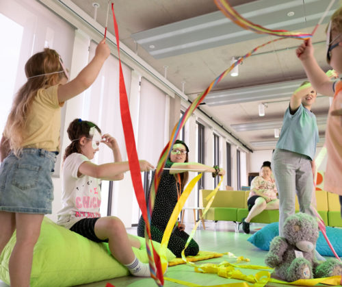 A group of children wave ribbons in a colourful room