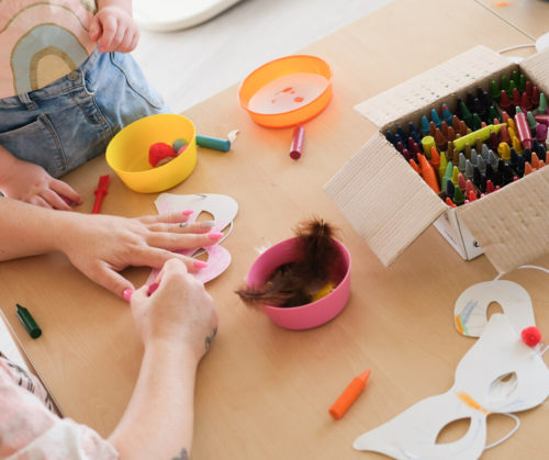 An adult's and a child's hands on a table with arts and crafts materials