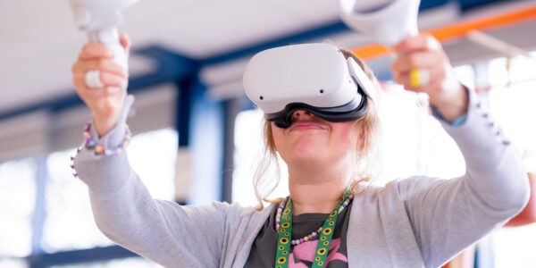 A young woman wearing a white VR headset waves her arms in the air. She is holding a white VR controller in each hand.