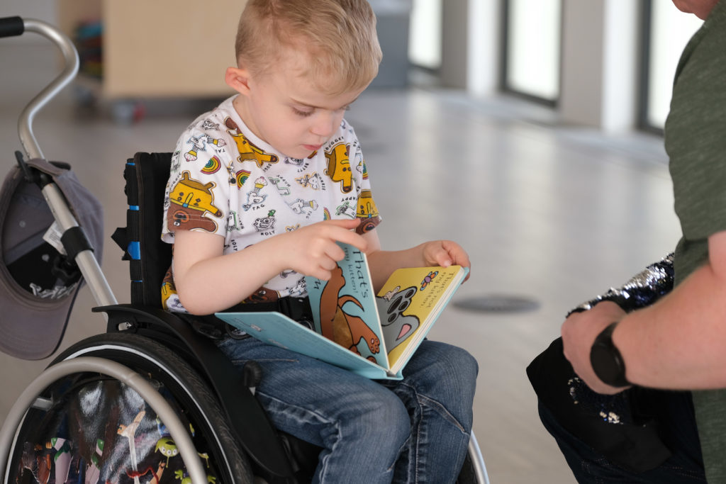 Thomas, a small boy with blonde hair, reading a book in his wheelchair.