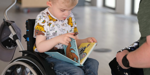 Thomas, a small boy with blonde hair, reading a book in his wheelchair.