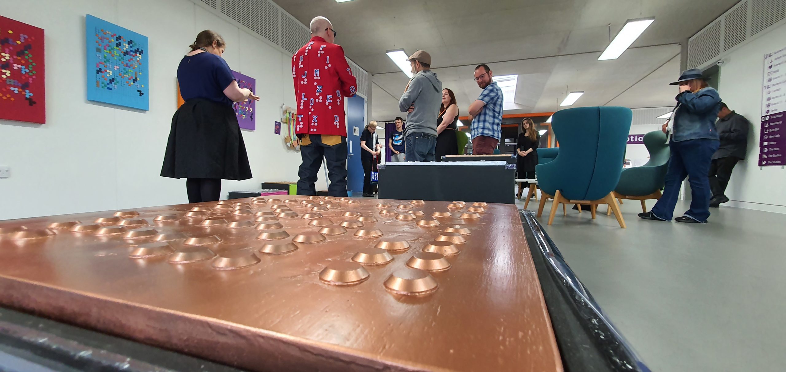 A copper metal sheet with raised dots in the foreground and a group of people in the background