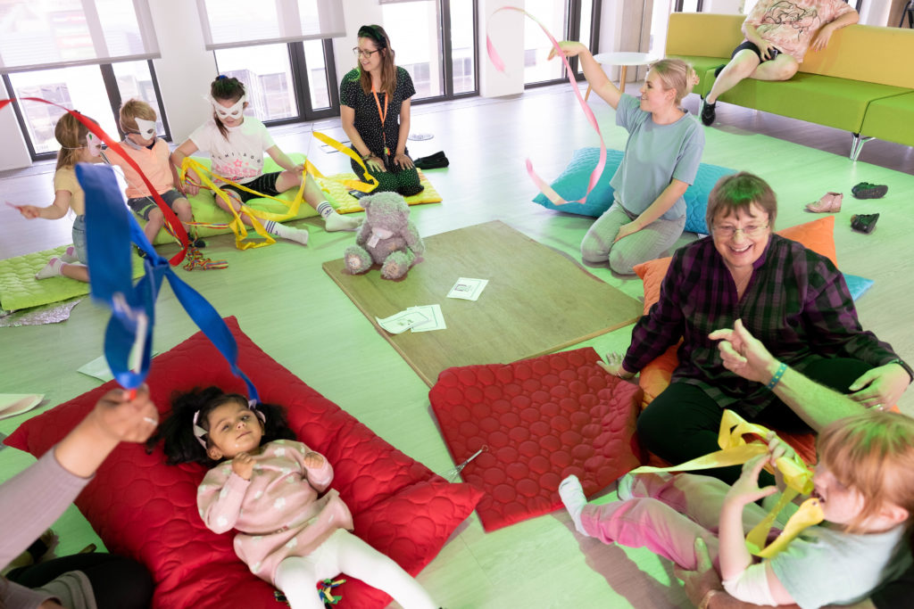 Five children and three support workers play with twirling ribbons in the TouchBase Pears family room.