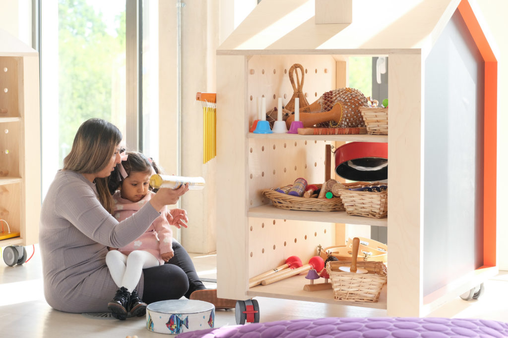An adult and child exploring a wooden house used for toy storage and play in the TouchBase Pears family room.