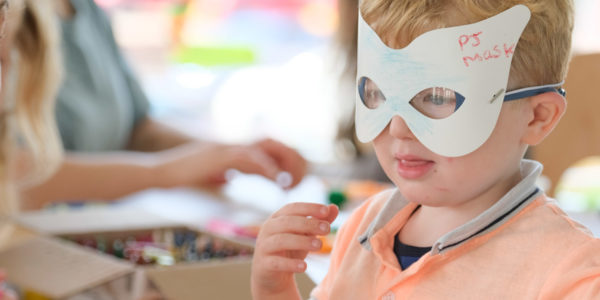 A young boy with blonde hair is wearing a home made paper mask.