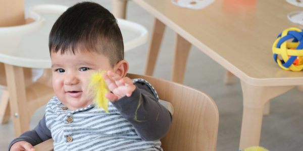 A young boy is sitting in a wooden high chair playing with yellow feathers.