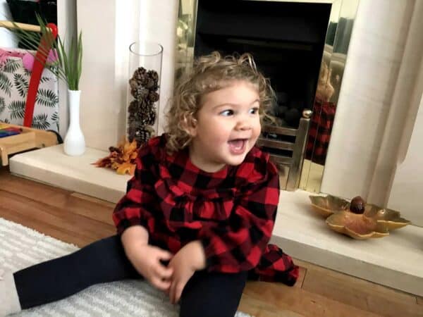 A little girl sits on a fireplace and smiles to someone to the right