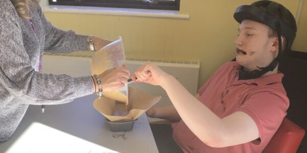 Luke mixing ingredients together in a bowl with help from his support worker.