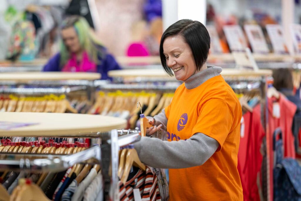A Sense volunteer smiles as she hangs clothes on a rail in a Sense shop