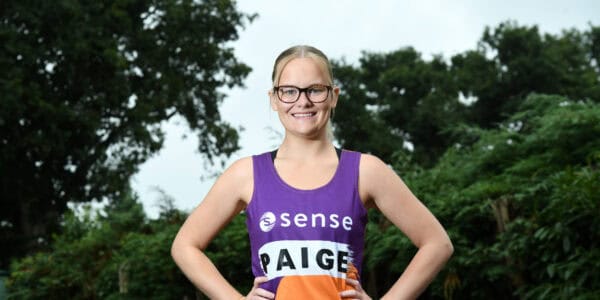 A young woman stands with her hands on hips, wearing her Sense marathon vest.