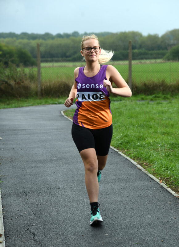 A young woman runs along a country road wearing her Sense marathon vest.