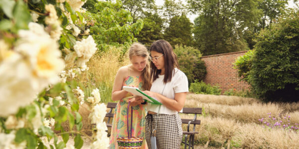 Two women standing in a garden look at a piece of paper together