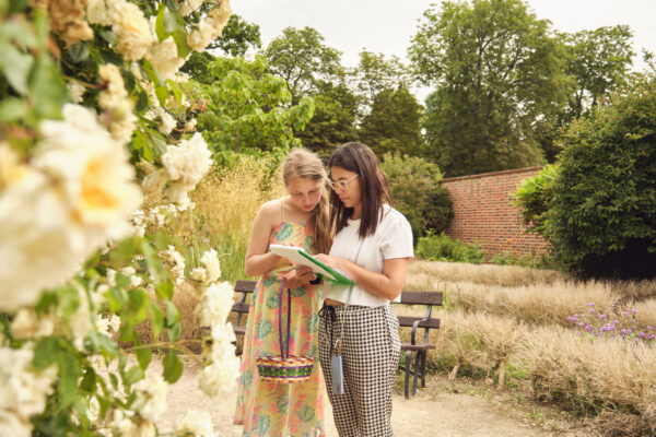 Two women standing in a garden look at a piece of paper together