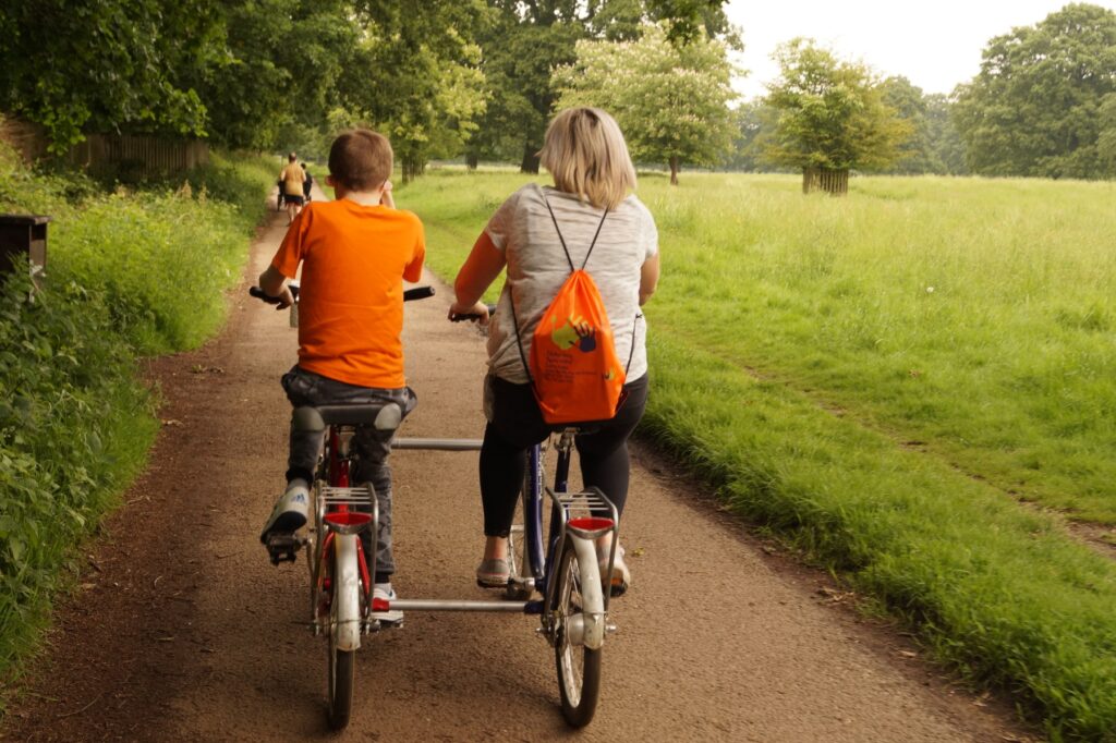 A woman and a young person riding on adapted bikes side-by-side, along a path surrounded by greenery.