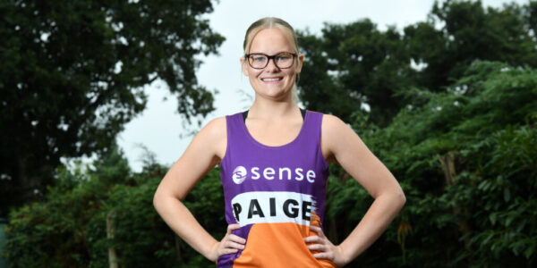 Paige, a blonde woman wearing glasses and a Sense running vest, smiling with her hands on her hips.
