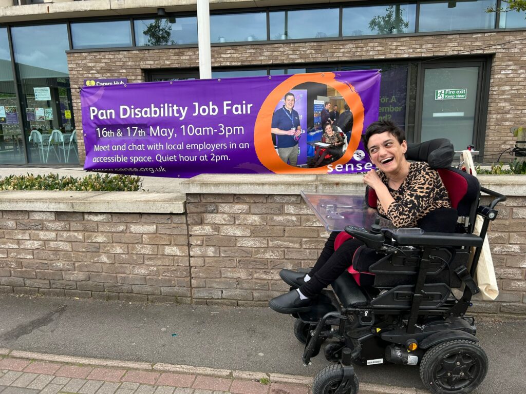A woman in a wheelchair next to a sign for the Sense Pan Disability Job Fair