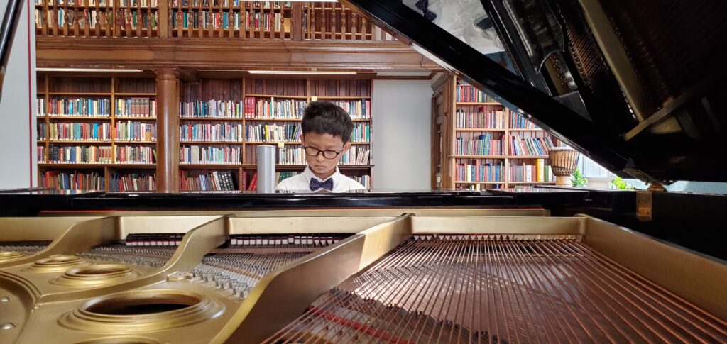 Chapman, a young Asian boy wearing glasses and playing the piano.