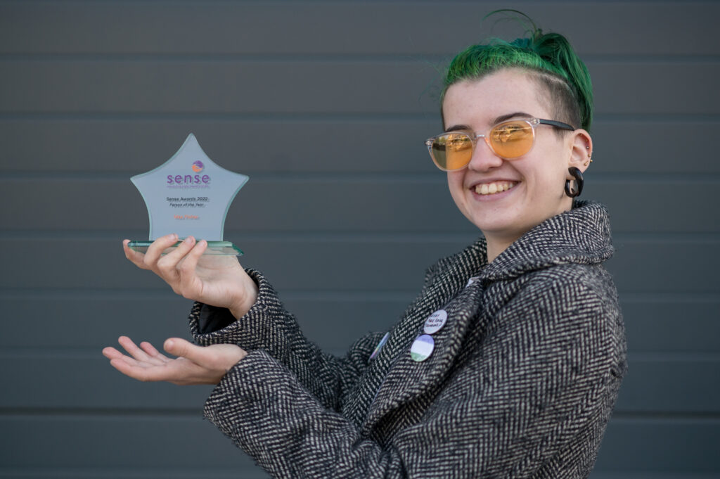 Max Fisher, a white genderqueer person with green hair, holding their Sense Award.