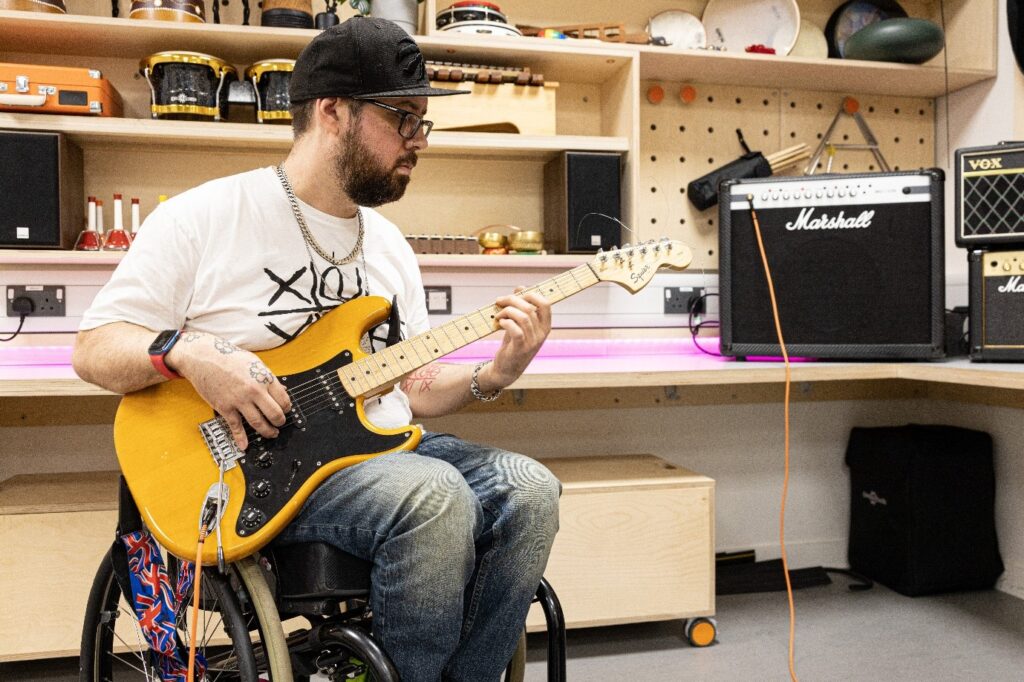 Kris Halpin, a white bearded man in a wheelchair, playing the guitar.