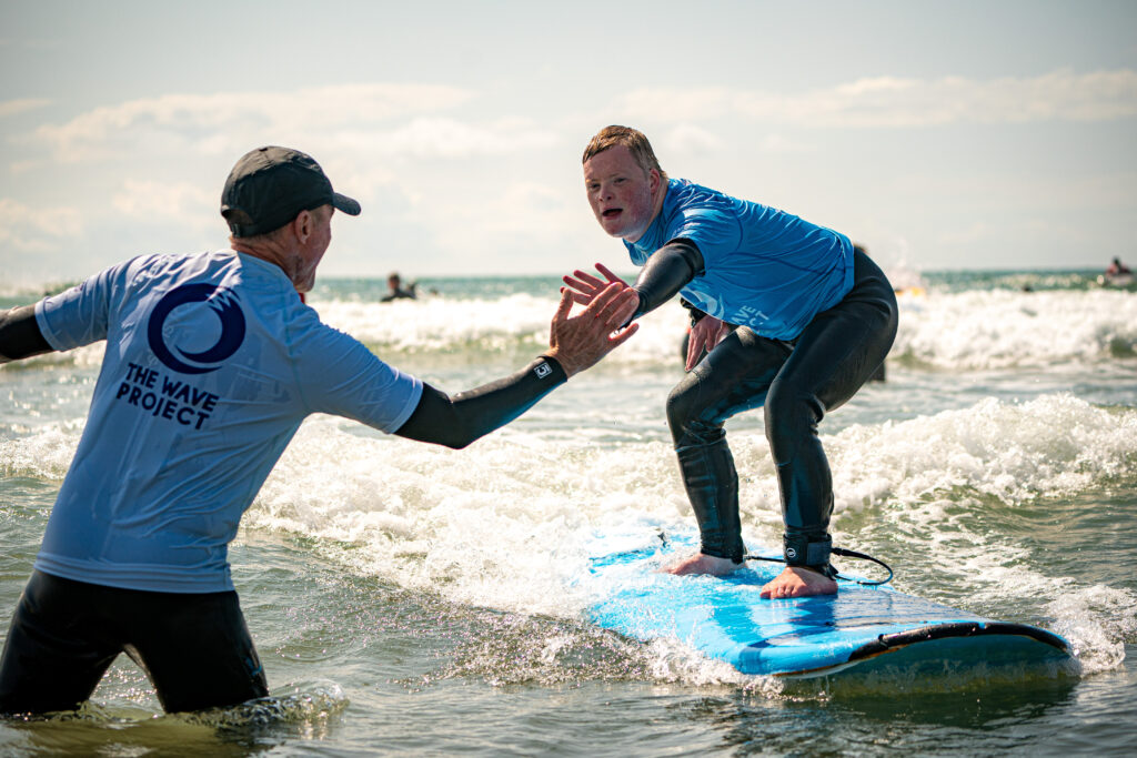 A young man in a wetsuit reached out to high five a member of The Wave Project team as he surfs past.
