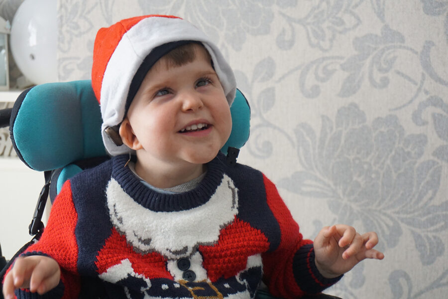 Luca sitting in his chair, smiling and wearing a Christmas hat.