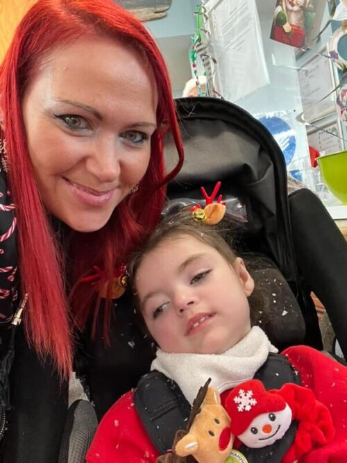 A smiling woman with long red hair moves close to her daughter who's sitting in her pram.