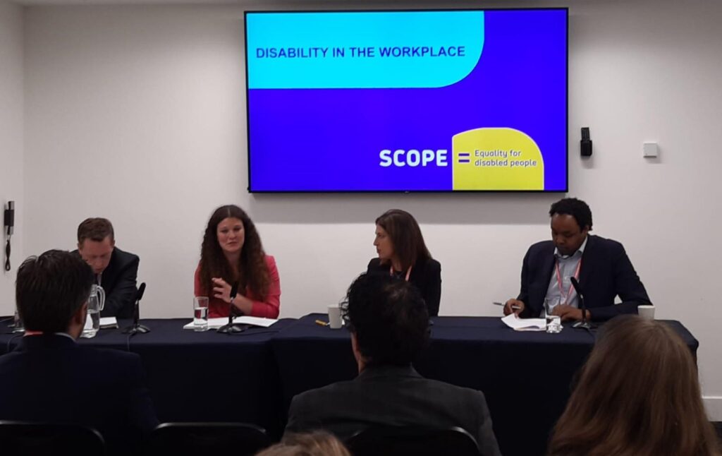 Four people sat at a table presenting at an event. The people are the minister for disabled people, Sarah from Sense and Louise and Abdi from Scope